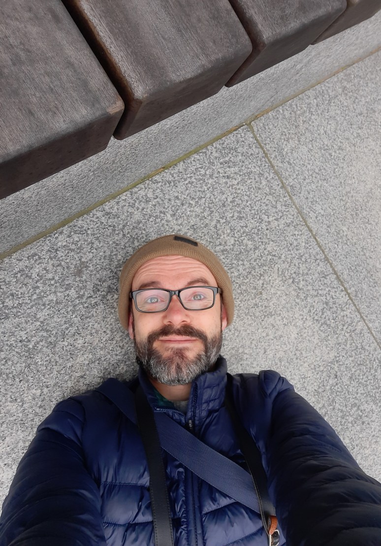 Photographer Mike Osborn flat on the pavement capturing Manchester's skyscrapers.